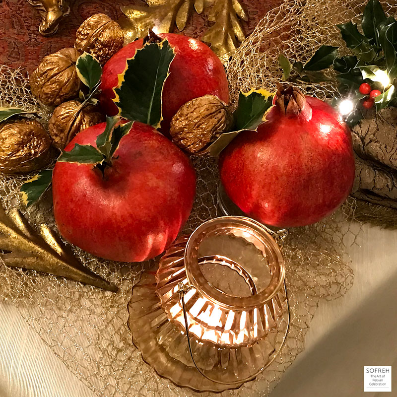 Shiny pomegranates and gold-finish walnuts with sprigs and leaves of holly and Christmas lights.